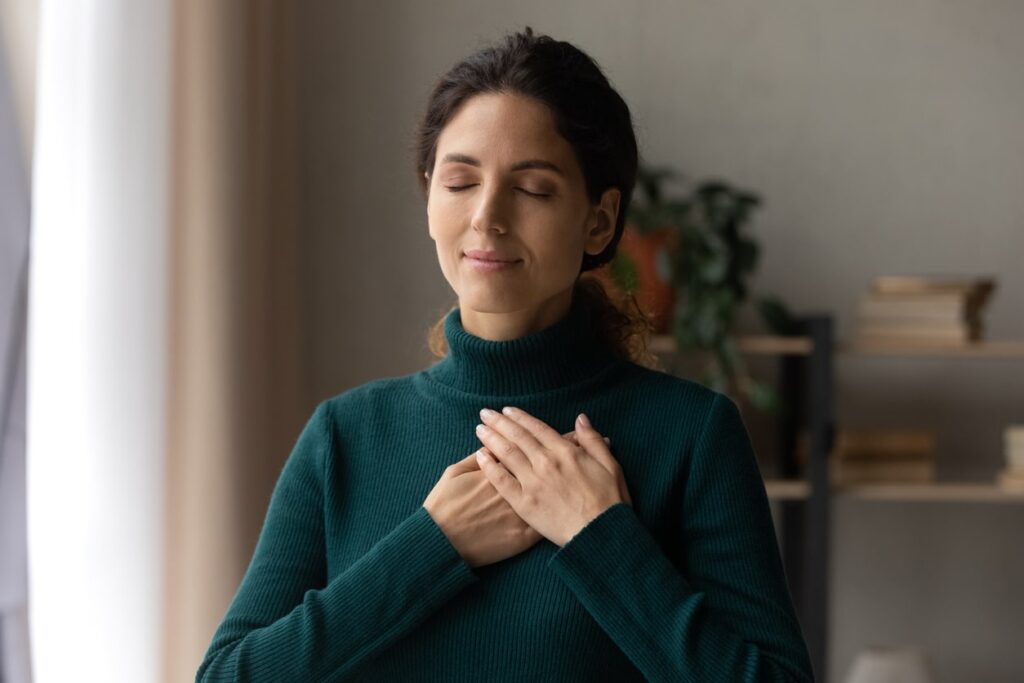 woman taking deep breath, eyes closed and hands over heart. feeling peaceful