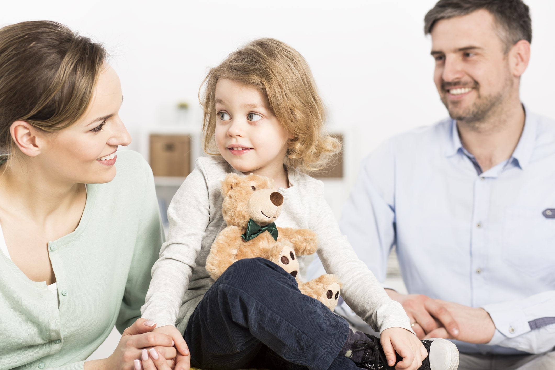 little girl holding teddy bear between mom and dad